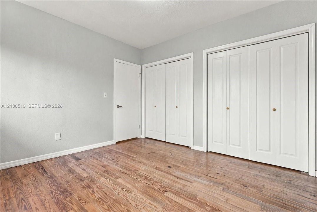 Wood-finish flooring featuring dual sets of white bi-fold closet doors and a single interior door