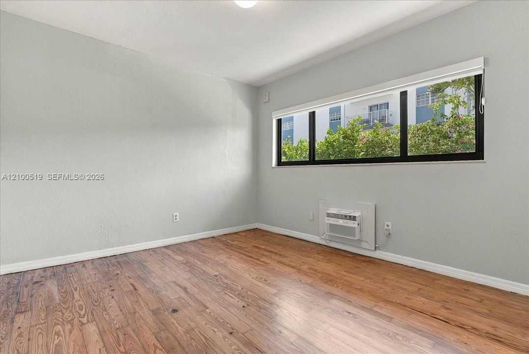 Interior room featuring wood-finish flooring, a large horizontal window with a black frame, and a wall-mounted air conditioning unit