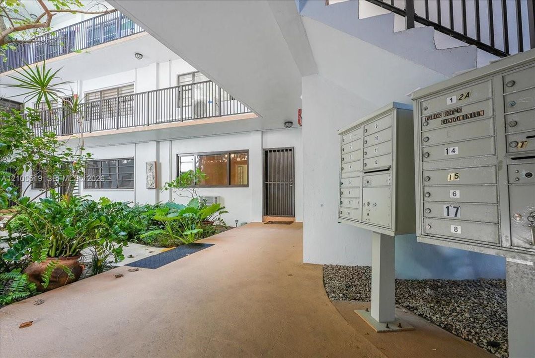 Exterior grounds featuring metal mailboxes, multi-level walkways with metal railings, and a landscaped courtyard with mature plantings