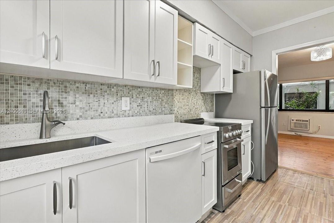 Kitchen featuring white shaker-style cabinetry, a mosaic tile backsplash, solid-surface countertops, an undermount stainless steel sink with a high-arch faucet, and stainless steel appliances