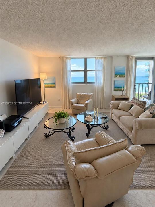 Living area featuring large windows, integrated storage cabinetry, neutral wall-to-wall carpeting, and a glass sliding door providing access to a balcony with ocean exposure