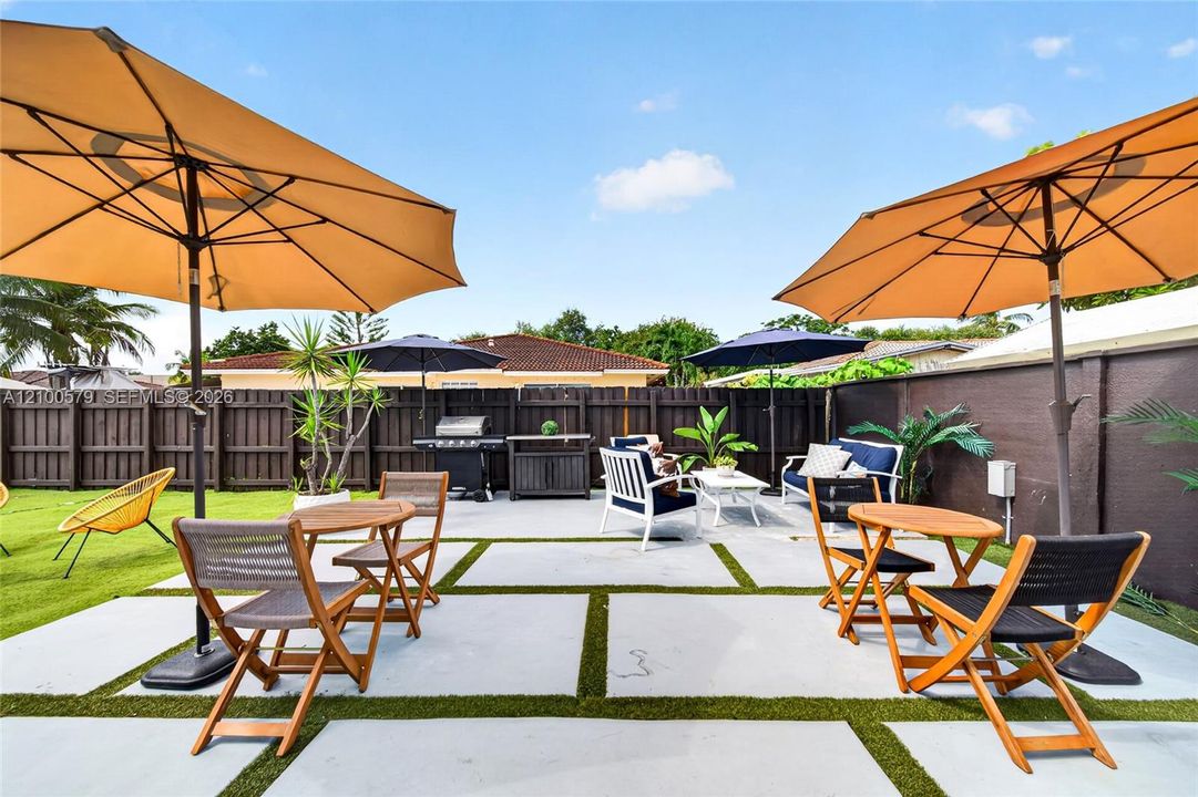 Rear patio featuring oversized concrete pavers with integrated artificial turf, enclosed by a dark wood privacy fence