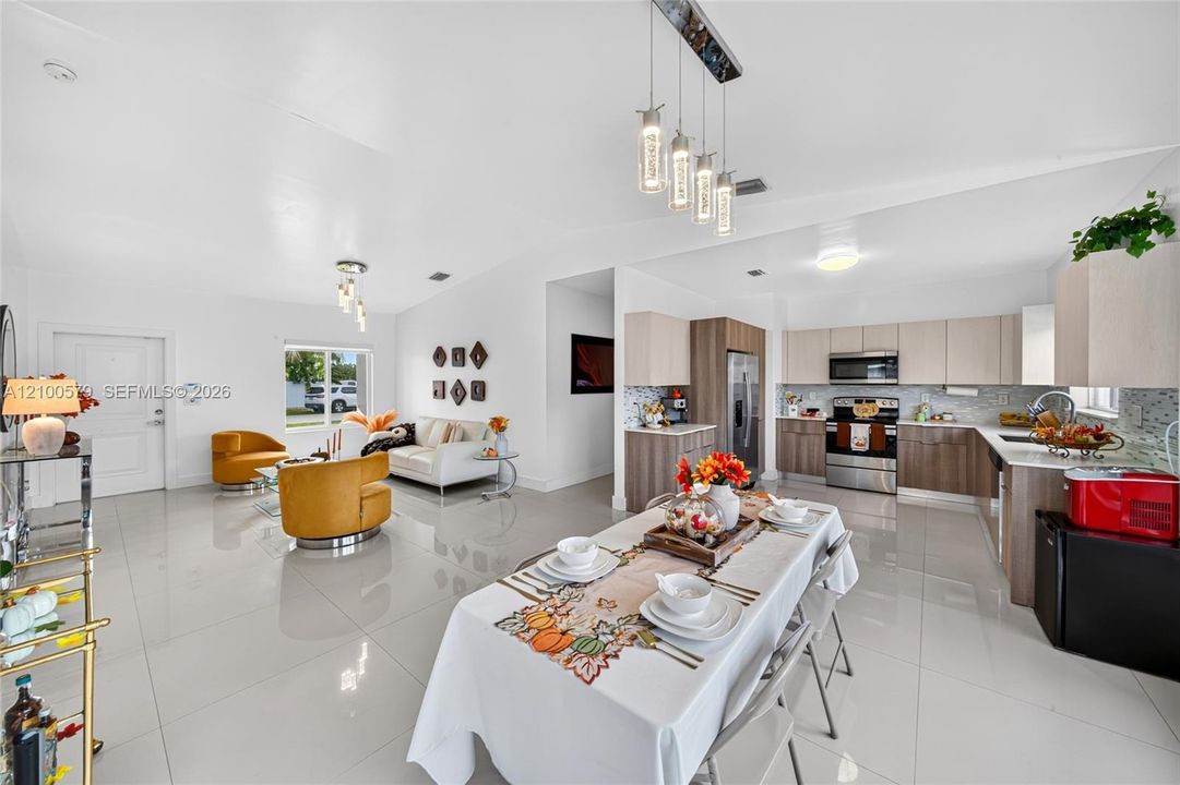 Open-concept interior featuring large-format tile flooring, vaulted ceilings, two-tone cabinetry with stainless steel appliances, and multi-pendant lighting fixtures