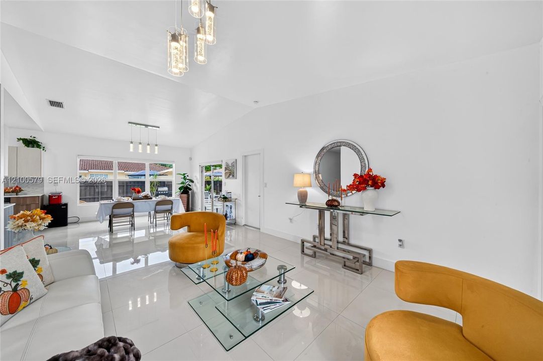 Open-concept interior featuring vaulted ceilings, polished tile flooring, multiple multi-light pendant fixtures, and sliding glass doors