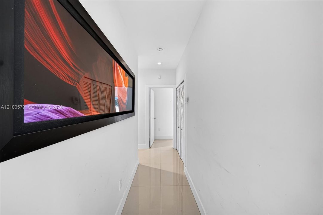 Hallway featuring neutral-toned tile flooring, recessed ceiling lighting, and louvered closet doors