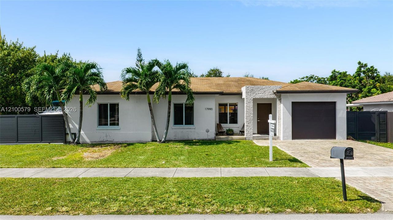 Single-story residence featuring a smooth stucco exterior, decorative stone facade accent, paved driveway, integrated garage, and privacy fencing