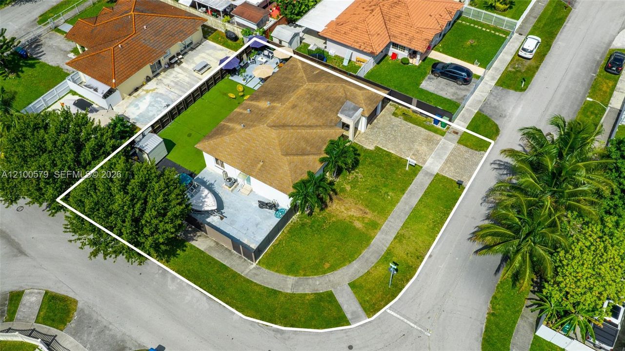 Corner lot property featuring a hip roof, paved driveway, concrete patio, and fenced perimeter