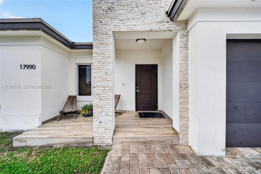 Exterior facade featuring a stone-veneer entryway, wood-finish flooring on the porch, a modern dark-toned front door, and a paver walkway