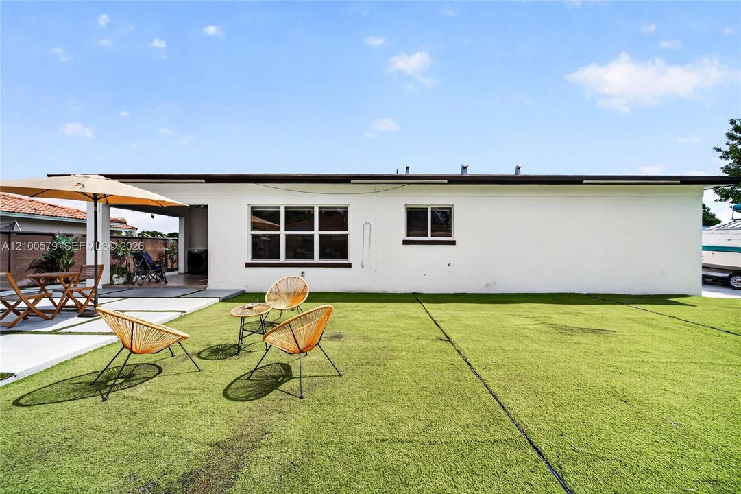 Backyard featuring a covered patio, concrete hardscaping, and synthetic turf lawn