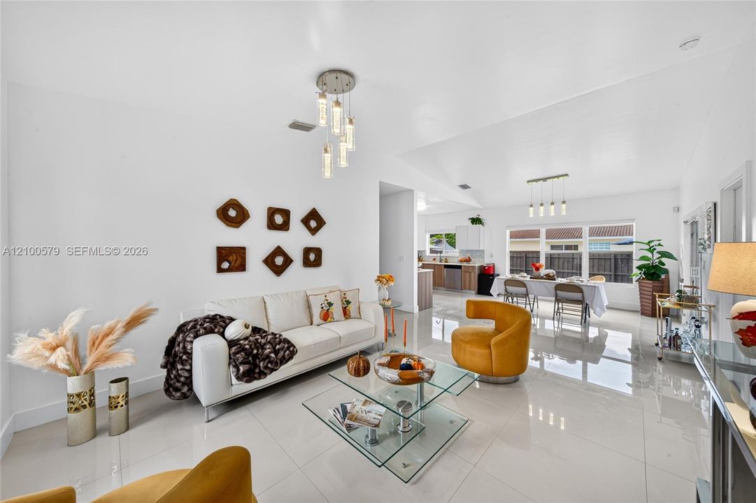 Open-concept interior featuring large-format tile flooring, vaulted ceilings, multi-pendant lighting fixtures, and expansive windows