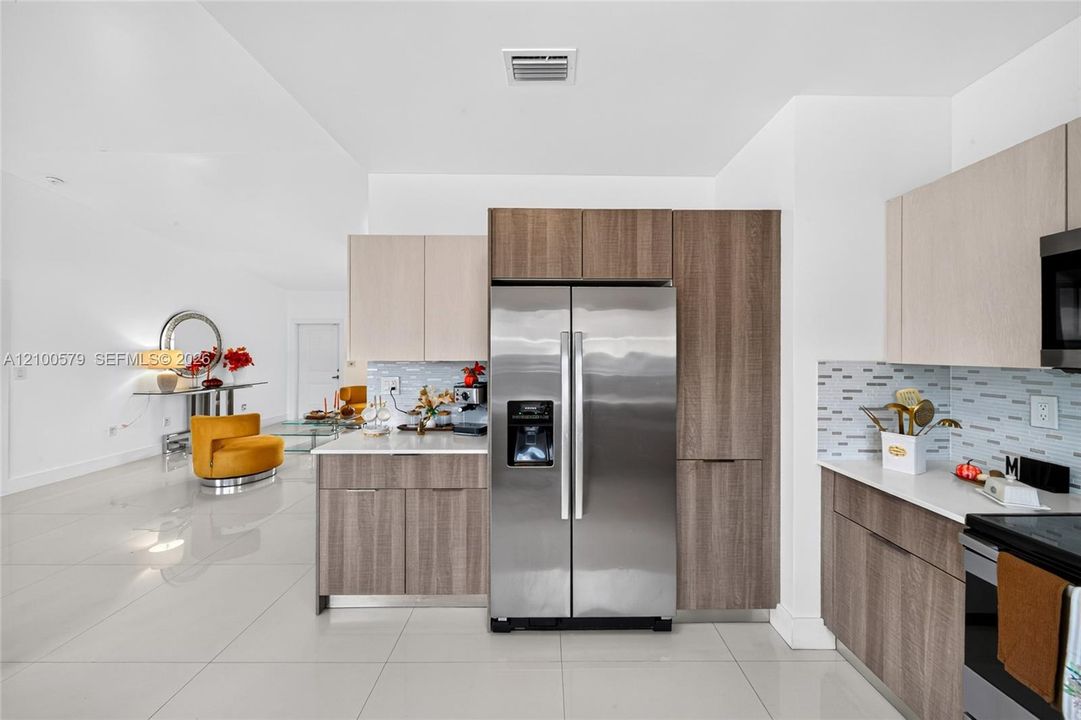 Kitchen featuring two-tone cabinetry, stone countertops, tiled backsplash, stainless steel appliances, and large-format flooring