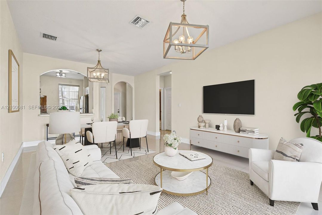 Open-concept living space featuring high ceilings, two geometric metal-frame chandeliers, architectural arched wall openings, and neutral tile flooring throughout