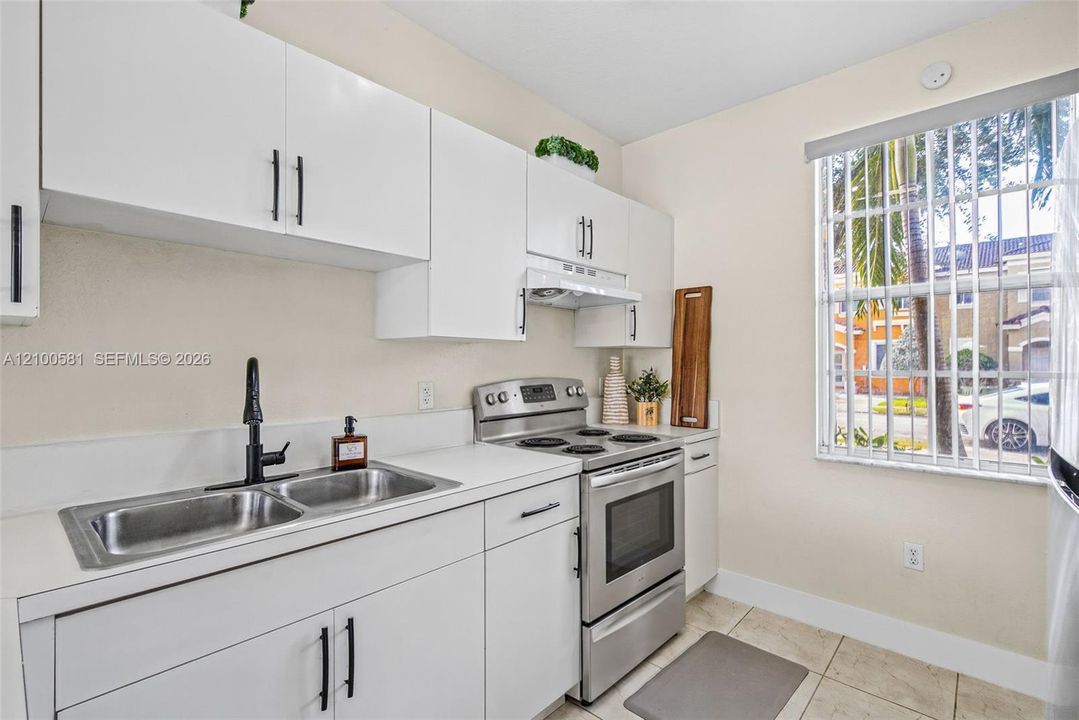 White cabinetry with matte black hardware, stainless steel electric range, dual-basin stainless steel sink with a matte black faucet, and tile flooring