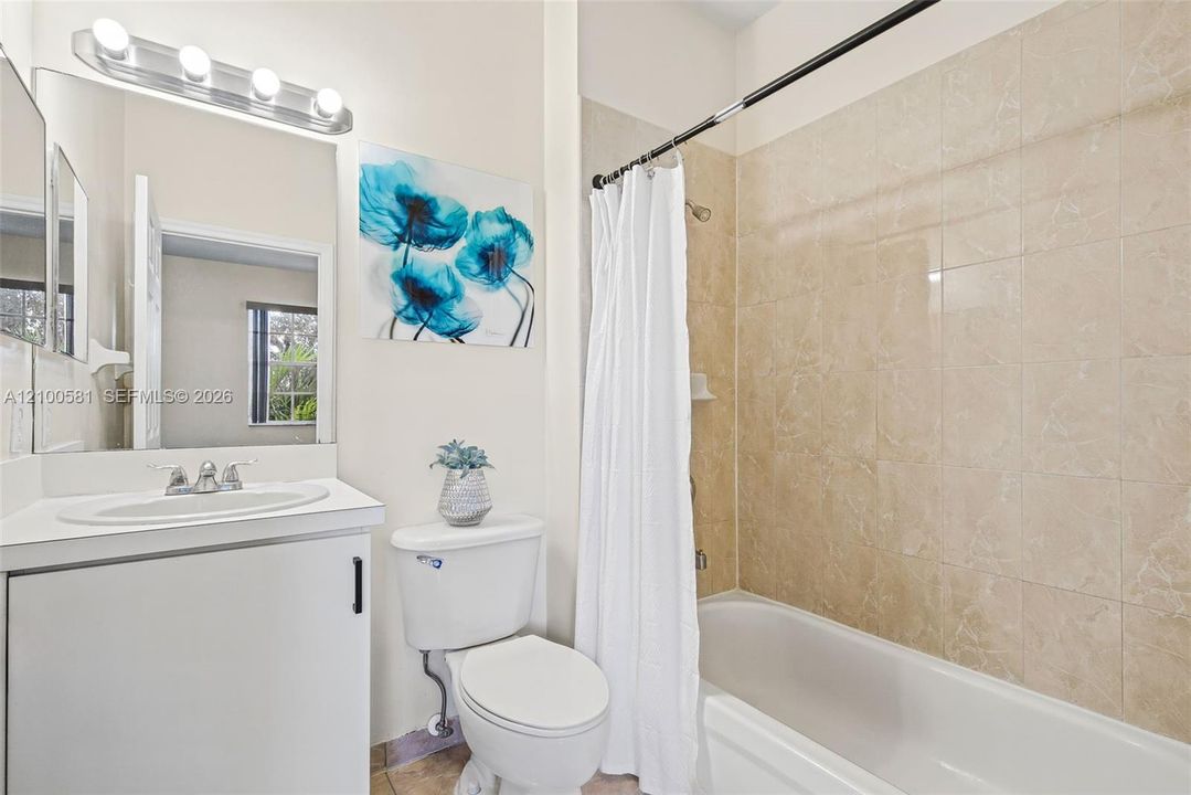 Bathroom featuring a white vanity cabinet with an integrated oval sink, four-light vanity fixture, and a tub-shower combination with full-height tile surround