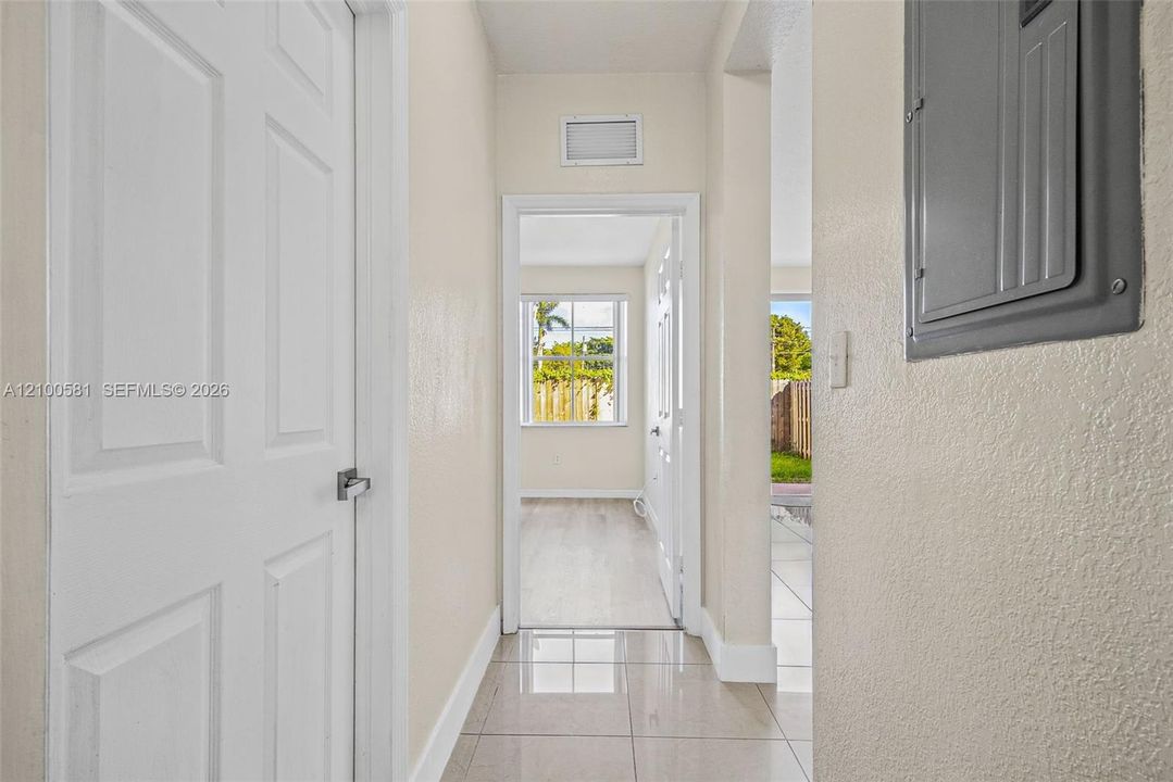 Neutral-toned interior featuring large-format polished tile flooring, white panel doors with modern hardware, and a wall-mounted electrical service panel
