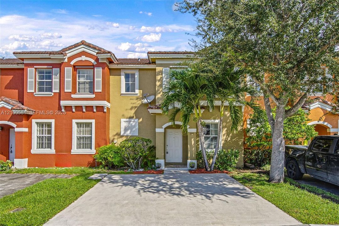 Two-story townhouse exterior featuring a concrete driveway, terracotta-style roof tiles, arched architectural details, and white-framed multi-pane windows