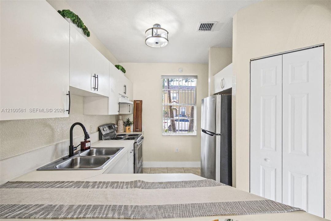 Kitchen featuring white cabinetry with matte black hardware, stainless steel refrigerator and range, dual-basin sink with a matte black faucet, and bifold closet doors
