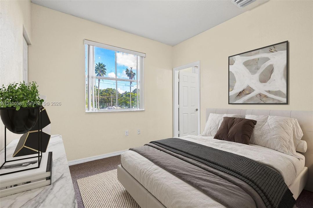 Bright secondary bedroom with abundant natural light from large window, neutral wall finishes, wood-finish flooring, and built-in closet with white door