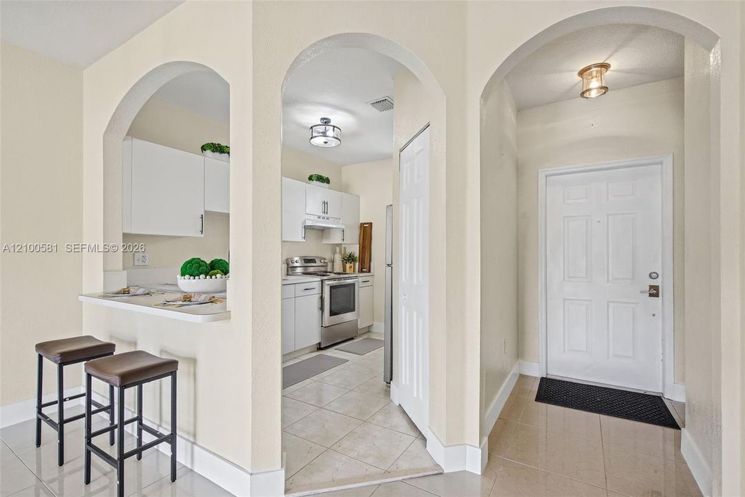 Interior entryway featuring arched architectural openings, ceramic tile flooring, a white six-panel door, and white shaker-style cabinetry with a built-in breakfast bar