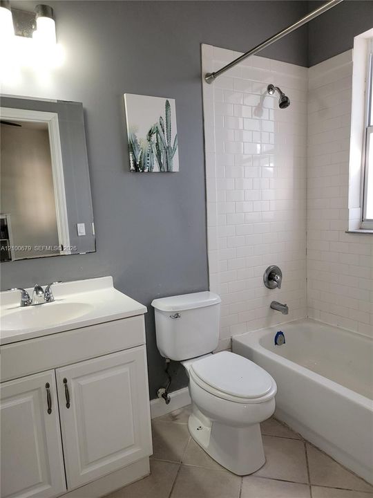 Bathroom featuring a white vanity cabinet, a shower-tub combination with white subway tile surround, a wall-mounted light fixture, and tile flooring