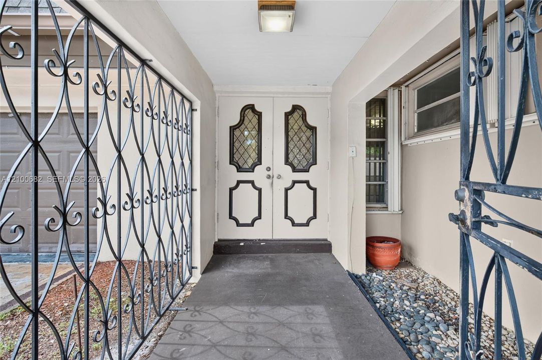 Double entry doors featuring leaded glass panes and decorative molding, protected by custom wrought iron security screening