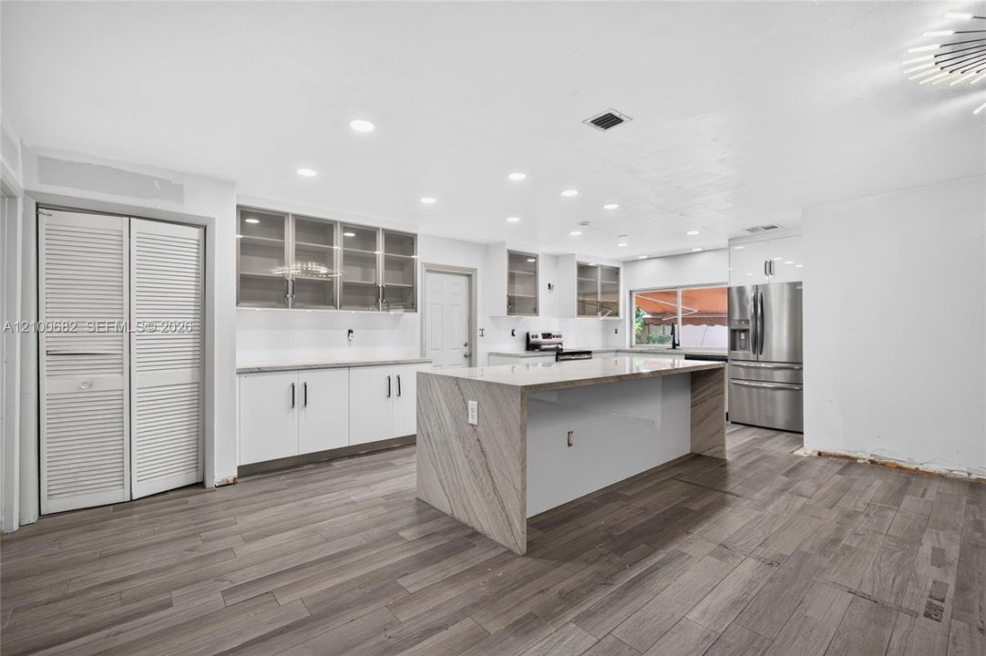 Kitchen featuring tiled wood-like flooring, quartz-surfaced countertops and taj majal island with waterfall edge, white cabinetry, glass-front upper cabinets, and recessed ceiling lighting