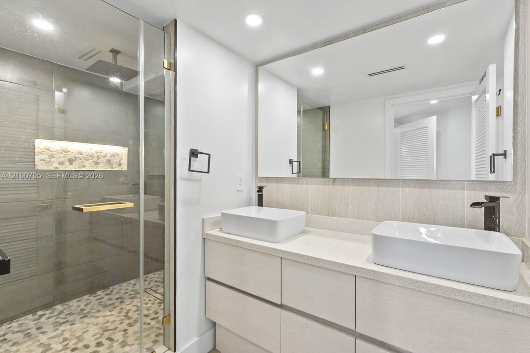 Double vanity featuring rectangular vessel sinks, stone-finish countertops, matte black fixtures, and a glass-enclosed shower with pebble tile flooring and a built-in stone niche