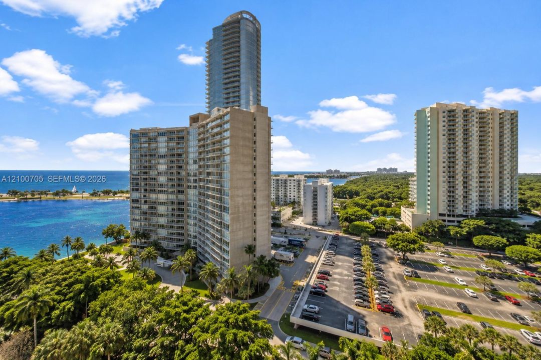 High-rise residential building featuring expansive glass balconies, concrete exterior cladding, and direct proximity to coastal waters and surrounding mature landscaping