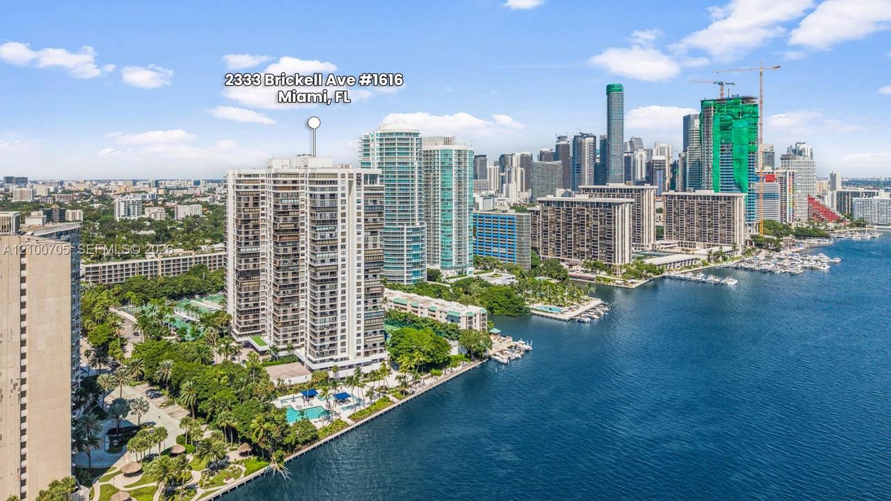 High-rise residential building featuring expansive waterfront positioning, a private swimming pool, mature perimeter landscaping, and immediate proximity to the Miami coastline