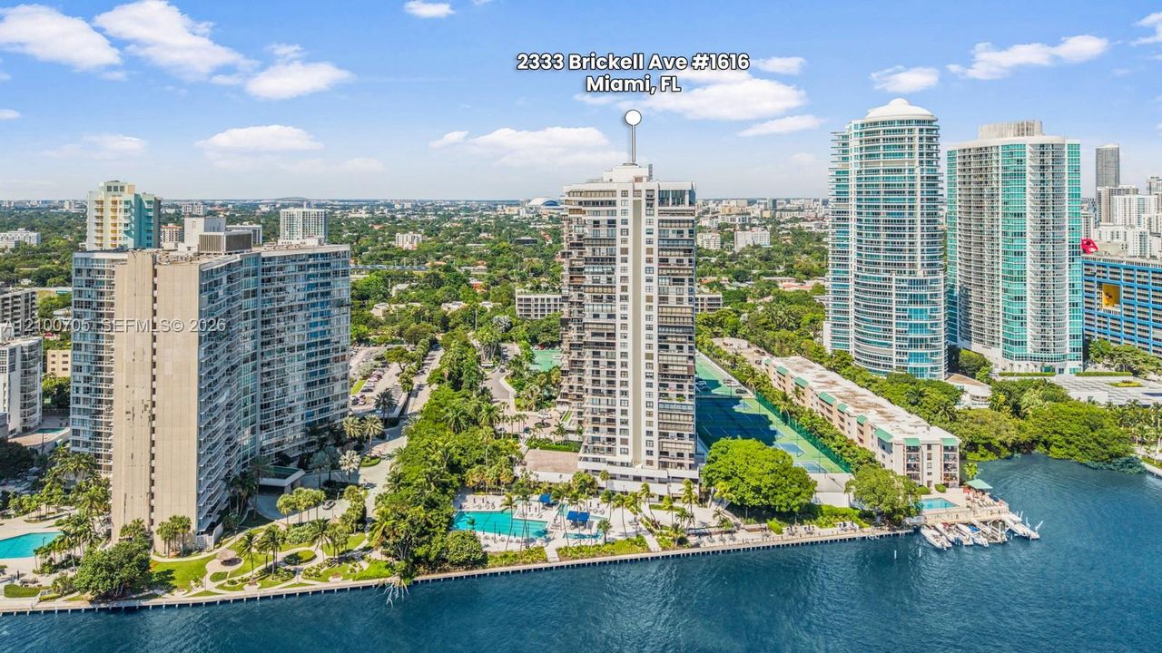 High-rise residential tower featuring a waterfront location, an outdoor swimming pool, paved walkways, mature landscaping, and a dock area