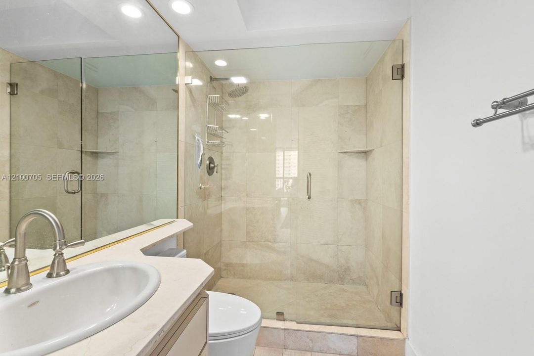 Walk-in shower with floor-to-ceiling neutral tile, glass enclosure, recessed lighting, and vanity with stone countertop