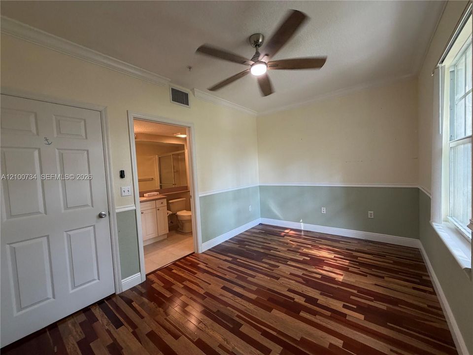 Interior room featuring wood-finish flooring, two-tone wall paint with chair rail molding, crown molding, and a ceiling fan with integrated lighting