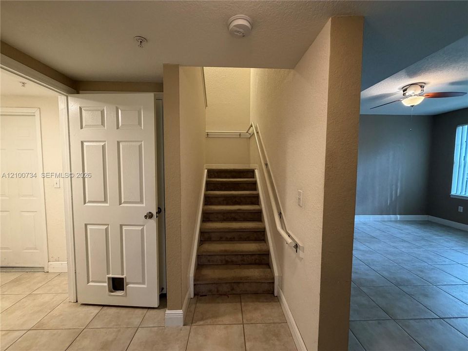 Staircase featuring carpeted treads, a wall-mounted handrail, and ceramic tile flooring