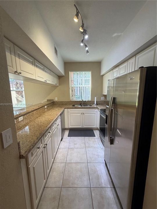 Kitchen featuring white cabinetry, stone-surface countertops, tile flooring, stainless steel side-by-side refrigerator, and track lighting