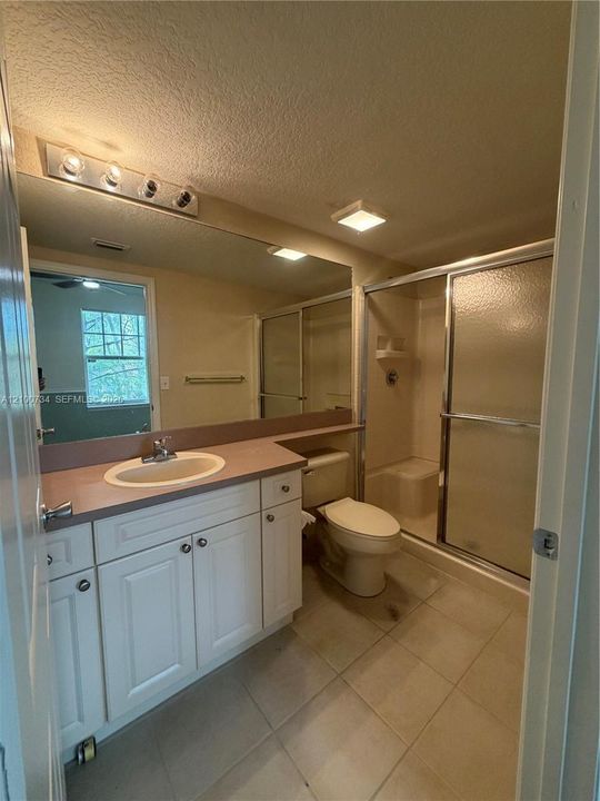 White vanity cabinetry with a solid surface countertop, an integrated oval sink, a full-width wall mirror, tile flooring, and a walk-in shower with sliding glass doors