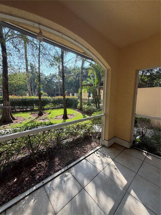 Screened-in patio with tiled flooring, arched architectural detailing, and metal fencing enclosing a landscaped lawn with mature trees