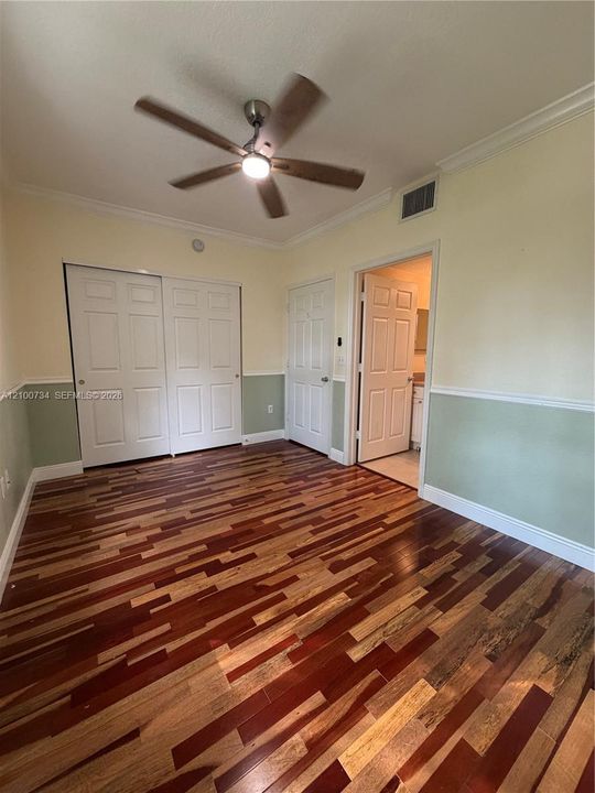 Wood-finish flooring, two-toned wall paint with chair rail molding, ceiling fan with integrated lighting, and dual-panel closet doors