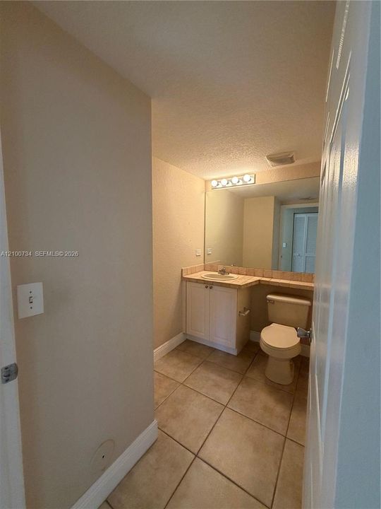 Bathroom featuring a vanity with integrated sink, stone-tile countertop, large wall-mounted mirror, four-light fixture, and ceramic tile flooring
