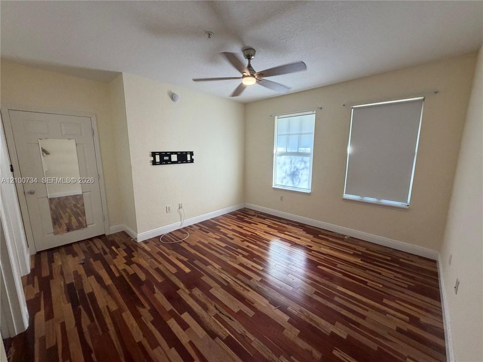 Room featuring wood-finish flooring, two windows with roller shades, and a ceiling fan with integrated light fixture