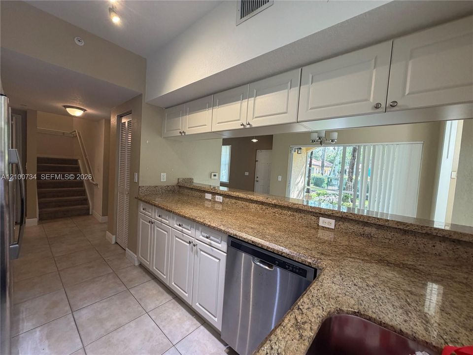 Kitchen featuring light-toned cabinetry, stone-surface countertops, full-width wall mirror, tile flooring, and stainless steel dishwasher