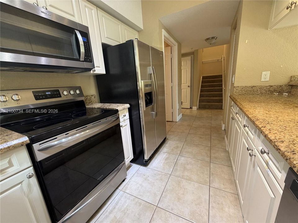 Kitchen featuring white cabinetry, stone-surface countertops, tile flooring, and stainless steel appliances