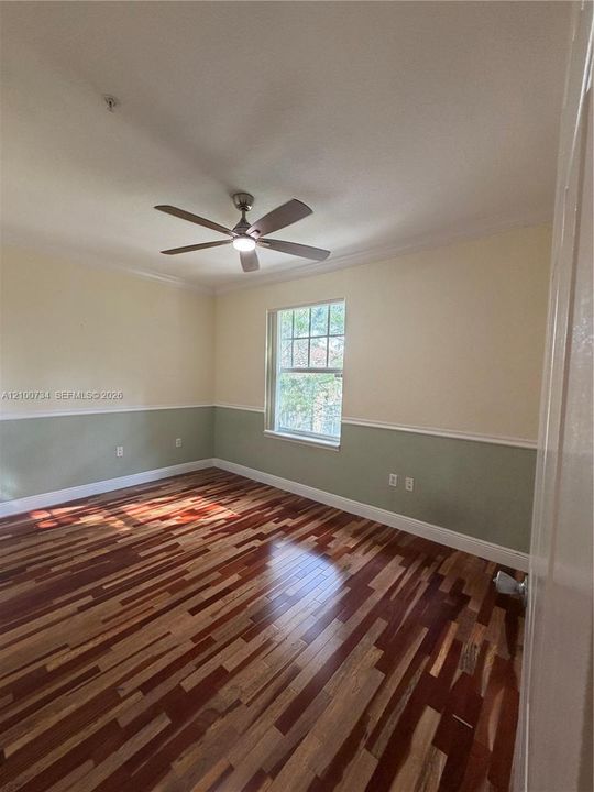 Room featuring wood-finish flooring, two-tone wall paint with a chair rail, a single-hung window, and a ceiling fan with integrated lighting