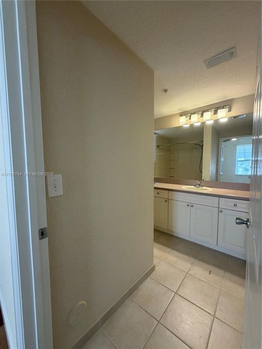 Bathroom featuring white cabinetry, solid-surface countertop with integrated basin, full-width vanity mirror, four-light fixture, and ceramic tile flooring