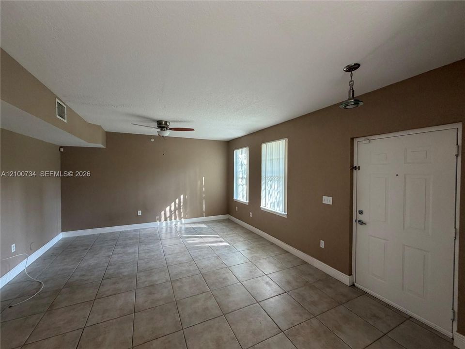Interior space featuring large-format ceramic tile flooring, neutral wall tones, multi-pane windows, a central ceiling fan, and pendant lighting