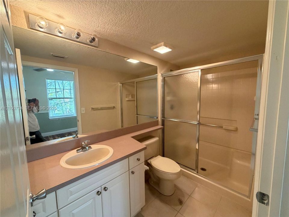 Bathroom featuring a solid-surface vanity countertop, white cabinetry with silver-tone hardware, a full-width wall mirror, and a shower enclosure with sliding glass doors