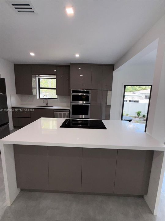 Kitchen featuring a central island with a waterfall countertop and integrated cooktop, flat-panel cabinetry, and stainless steel built-in double ovens