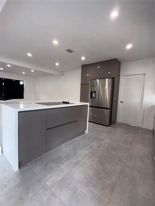 Modern kitchen featuring a central island with a waterfall countertop, high-gloss flat-panel cabinetry, stainless steel French-door refrigerator, and large-format tile flooring