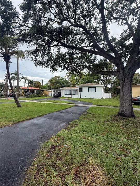 Single-story residence featuring a painted masonry exterior, covered carport, asphalt driveway, and mature landscaping