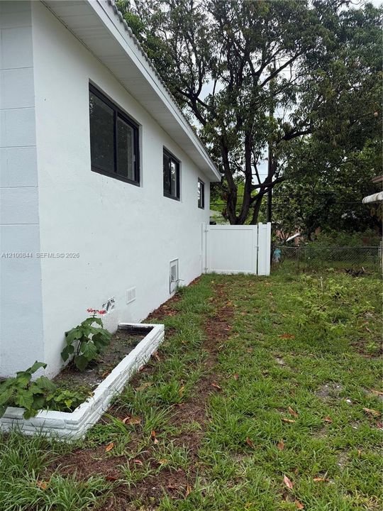 Stucco exterior featuring black-framed windows, a built-in raised brick planter, and a white vinyl privacy gate