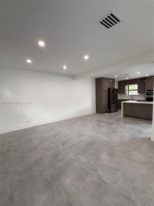 Large-format grey tile flooring, recessed ceiling lighting, glossy flat-panel cabinetry, and a kitchen island with stone-surface countertops